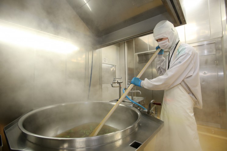 オーケーズデリカ調理製造部門での作業風景。白衣の人物が大釜で調理しています